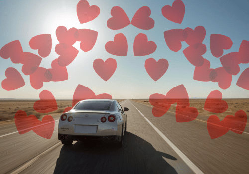 Silver sports car driving on an open desert road with heart graphics in the sky.
