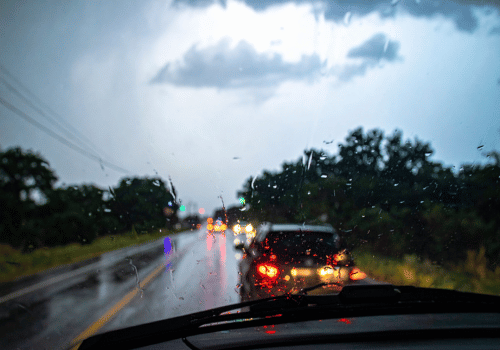Rainy road, with cars and headlights reflecting on wet pavement, seen through a windshield.