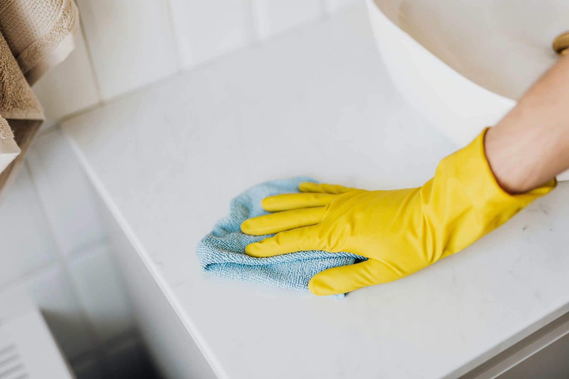 A person wearing yellow gloves is cleaning a toilet with a cloth.
