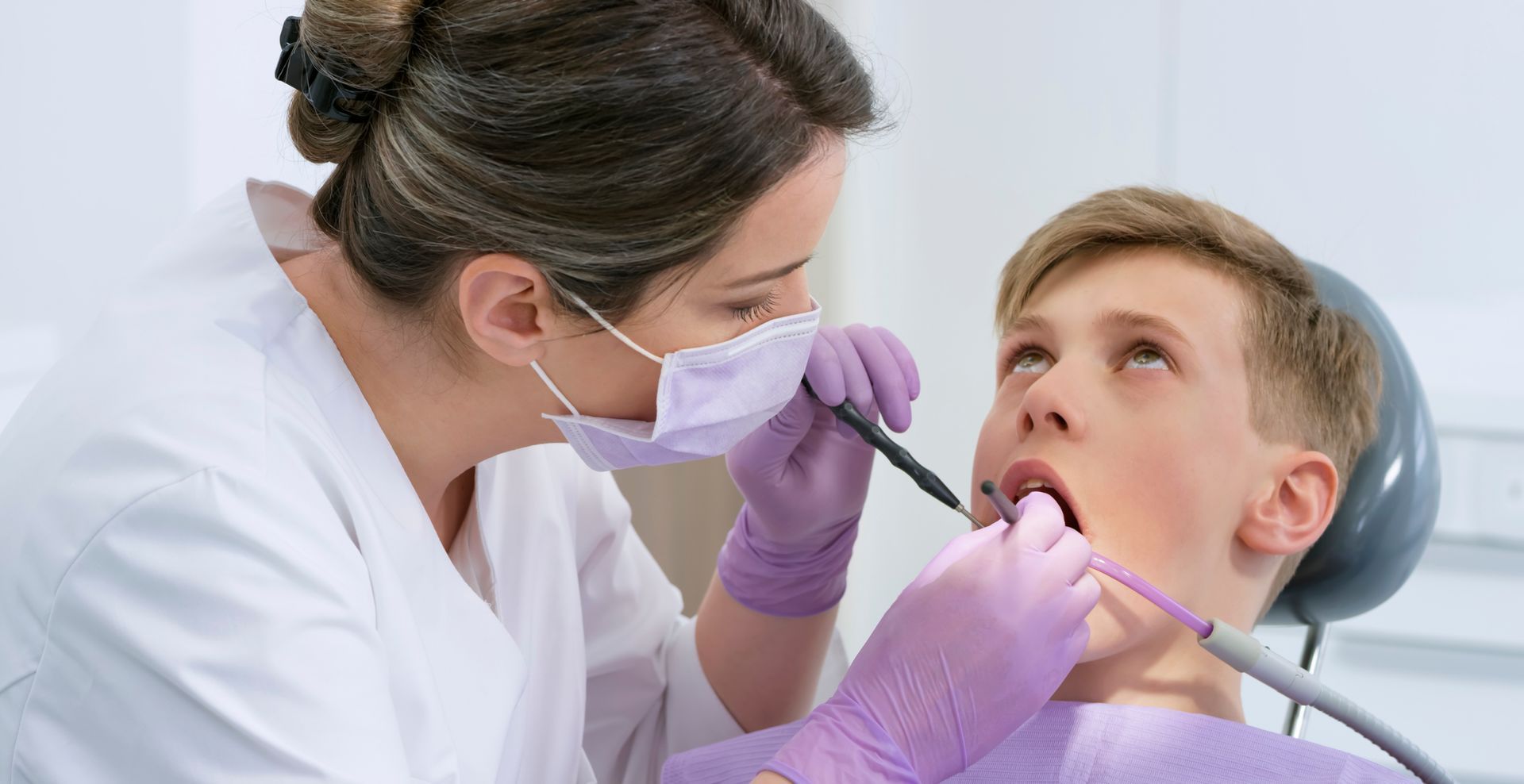 Dentist checks the mouth of a boy in a dentist office, as she repairs a tooth in his mouth. Dentist checks the mouth of a boy in a dentist office, as she repairs a tooth in his mouth.