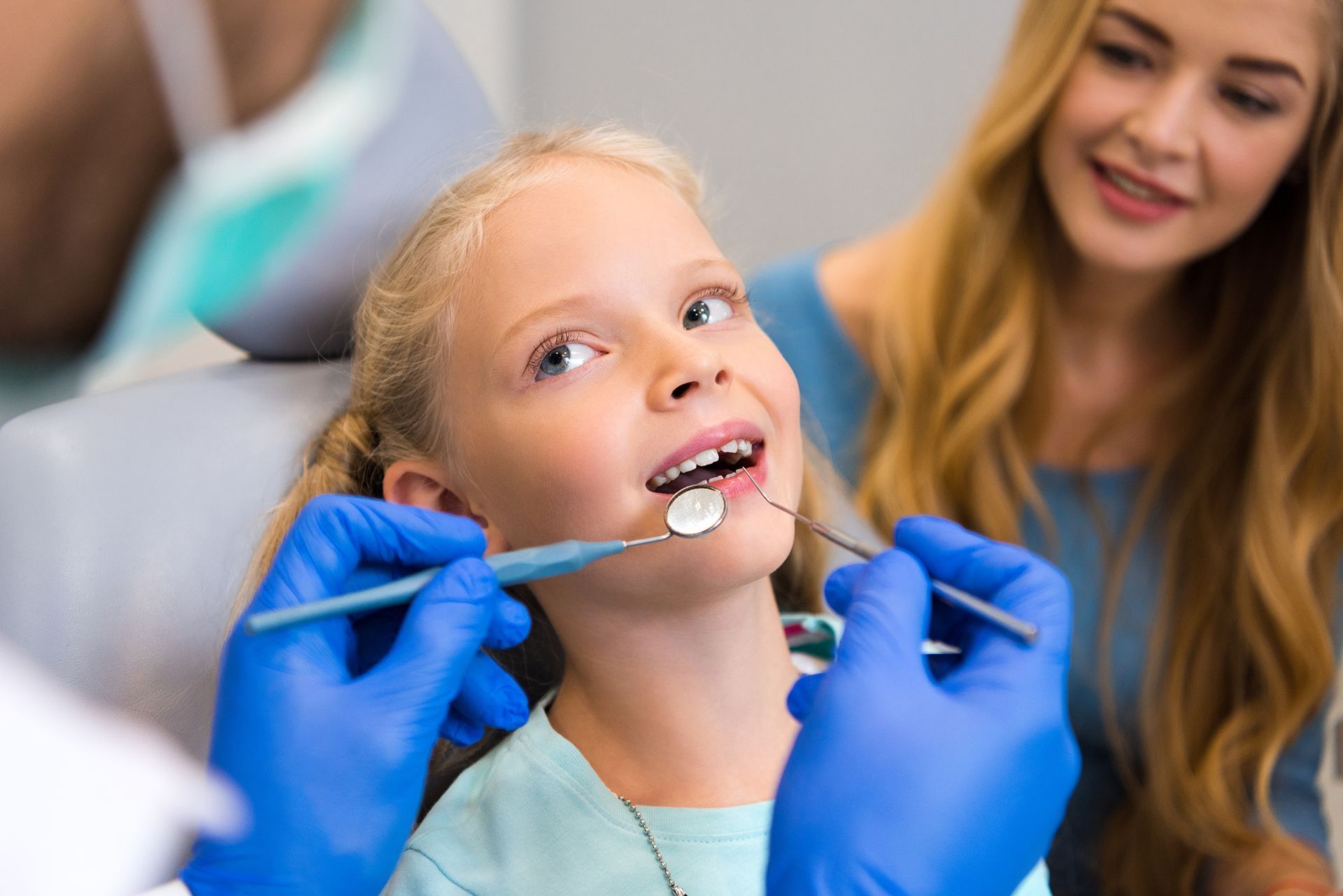 Shot from the back of a dentist working with a young girl, sitting next to her mother.