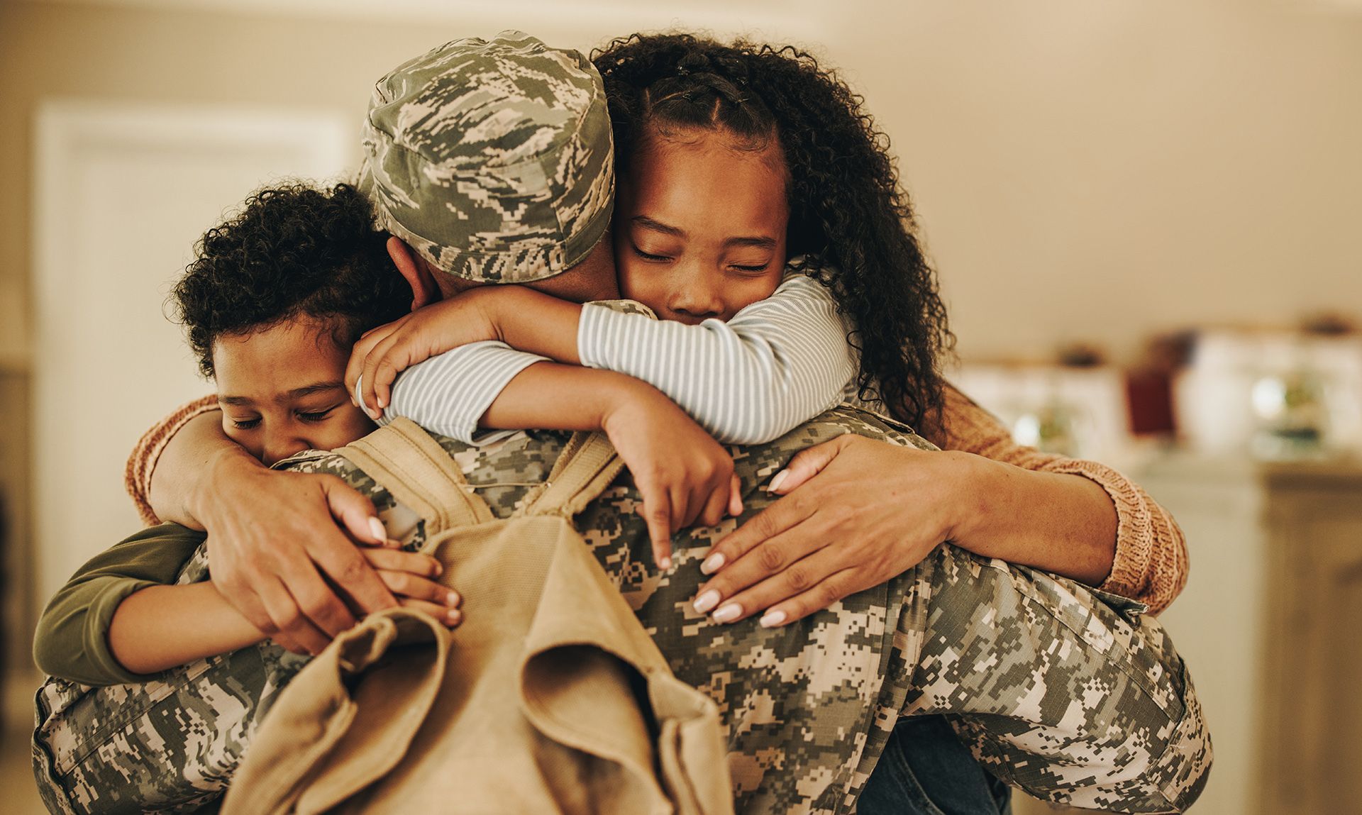 a man in a military uniform is hugging his wife and two children .