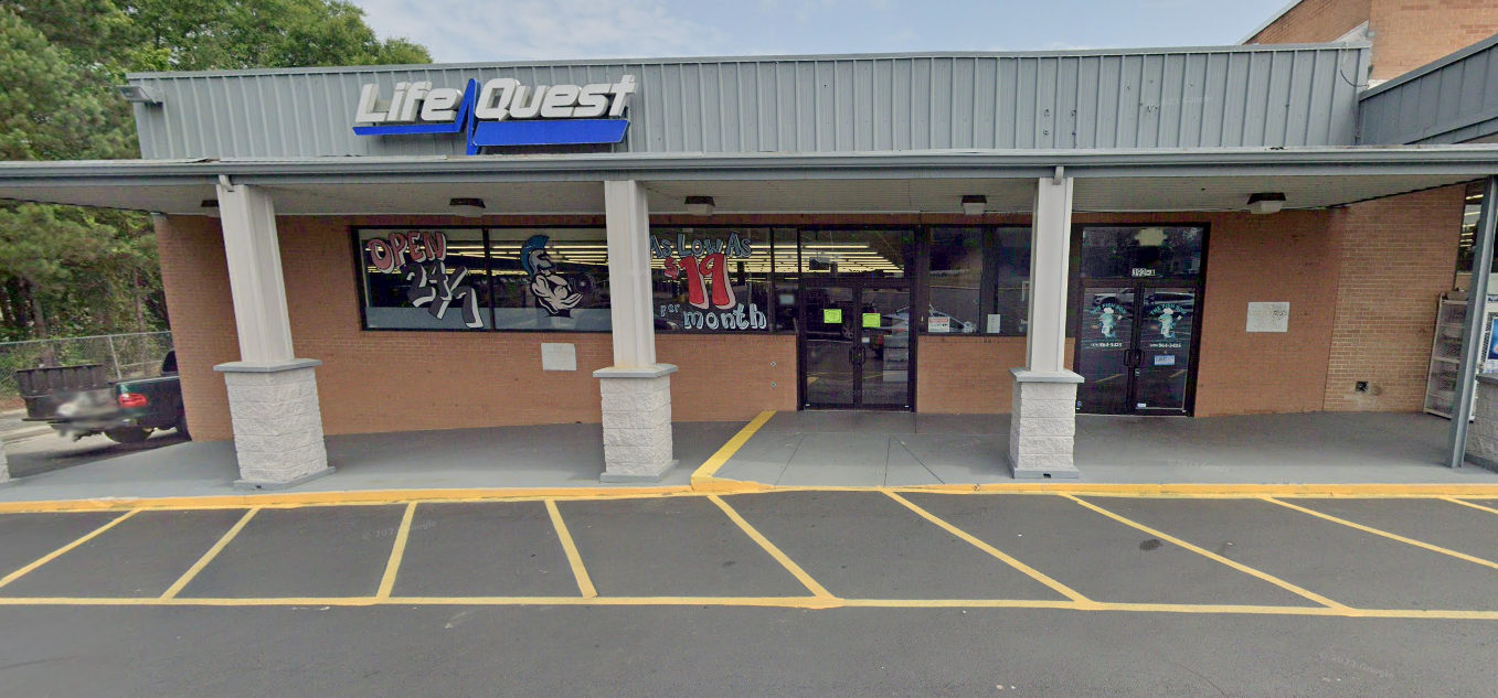 Exterior view of Life Quest store with glass windows, gray awning, and brick facade. Yellow parking lines are visible.