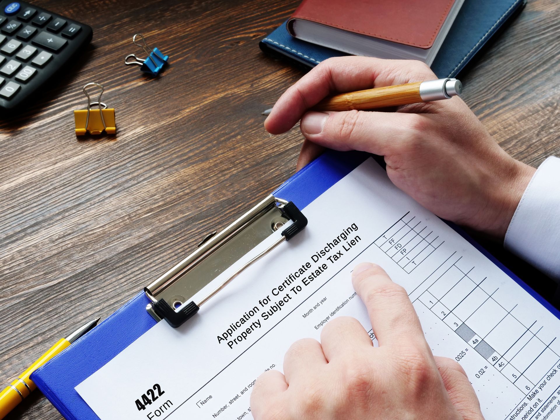 Person filling out a tax form at a desk with a calculator and notepad.
