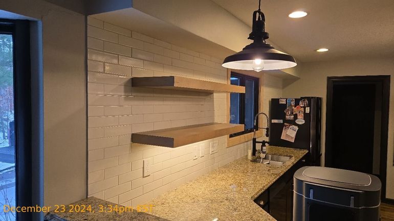 Modern kitchen with white brick backsplash, granite island, pendant light, and open shelves.