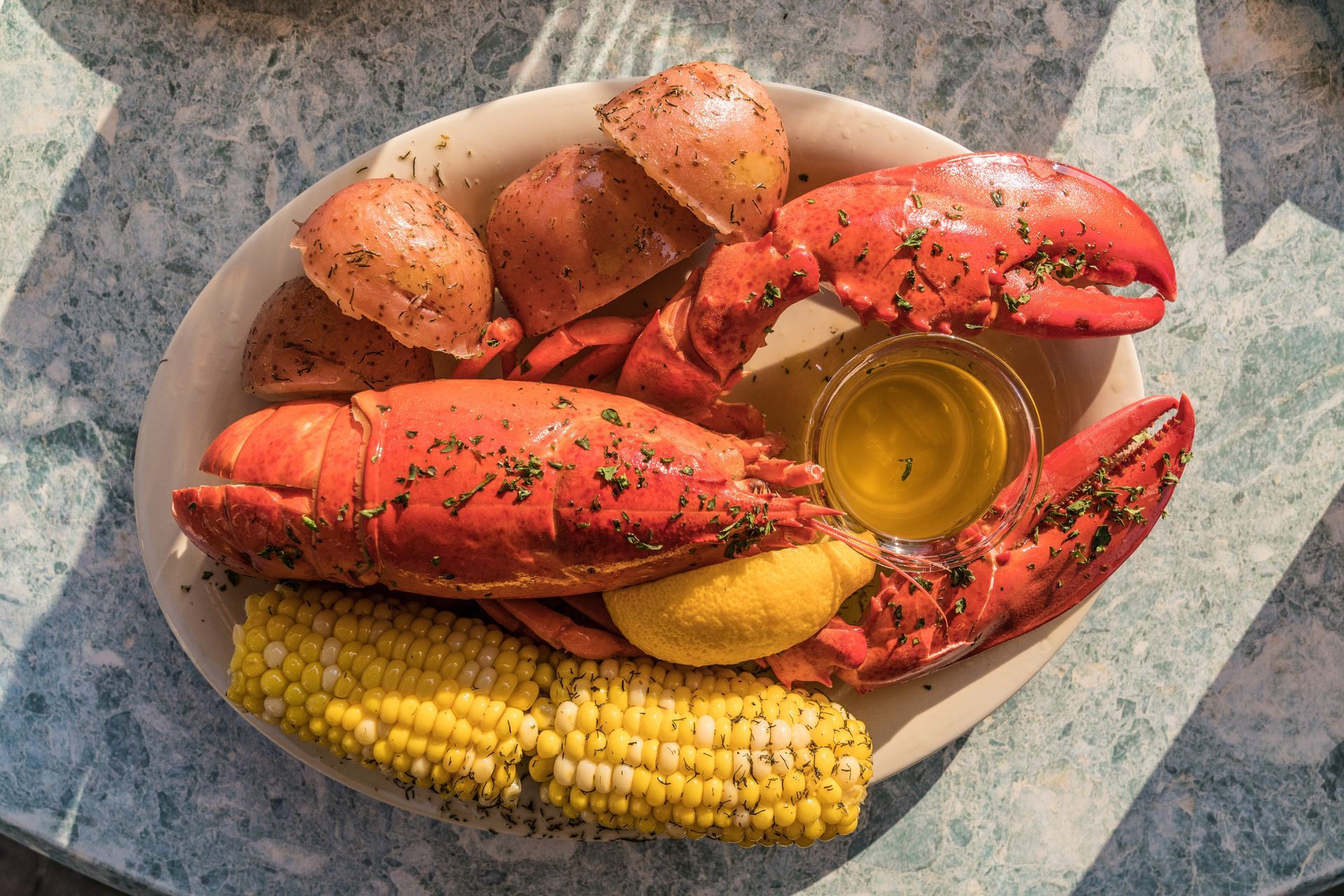 A plate of lobster , corn on the cob and potatoes on a table.