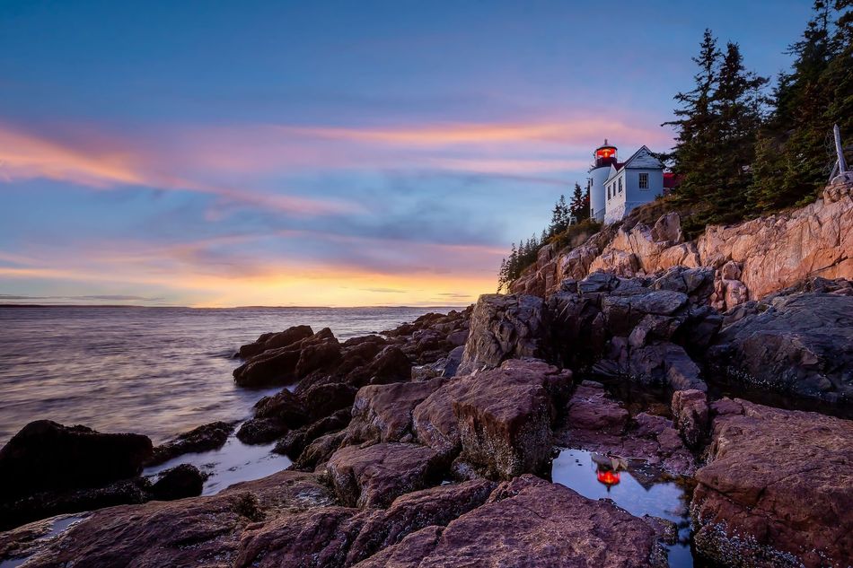 A lighthouse on a rocky cliff overlooking the ocean at sunset.