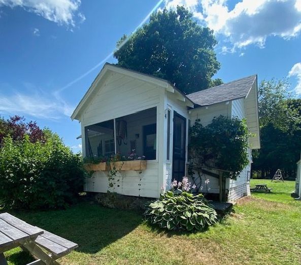 A small white house with a screened in porch and a picnic table in front of it.