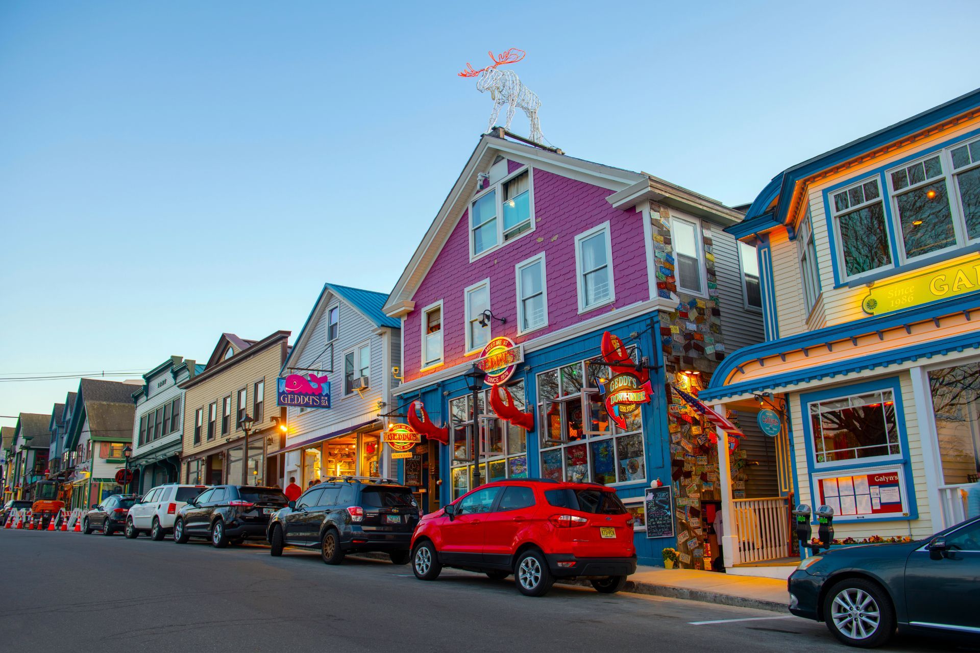 A red car is parked in front of a row of colorful buildings.