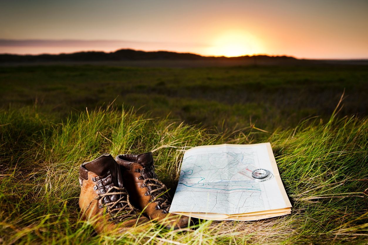 A pair of boots with a map and a compass in the grass.