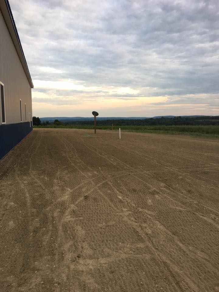 A dirt road leading to a building with a tree in the distance.