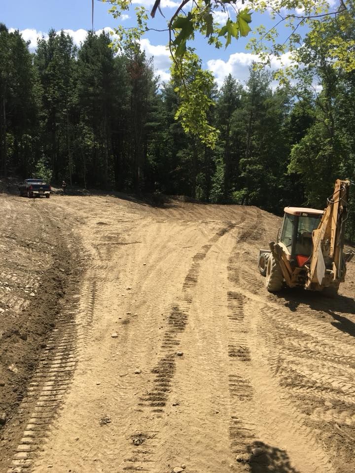 A bulldozer is driving down a dirt road in the woods.