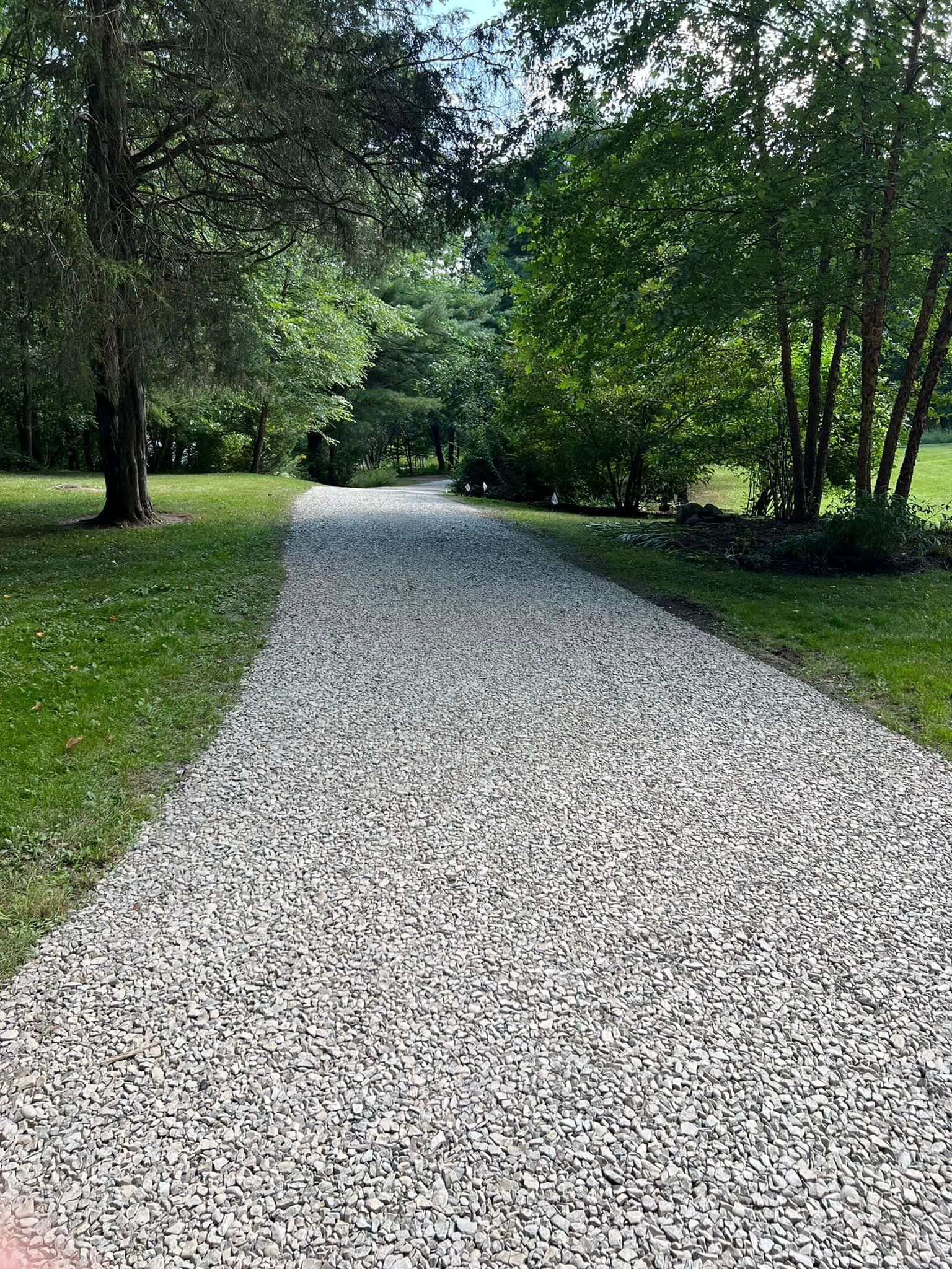 A gravel driveway leading to a grassy field surrounded by trees.