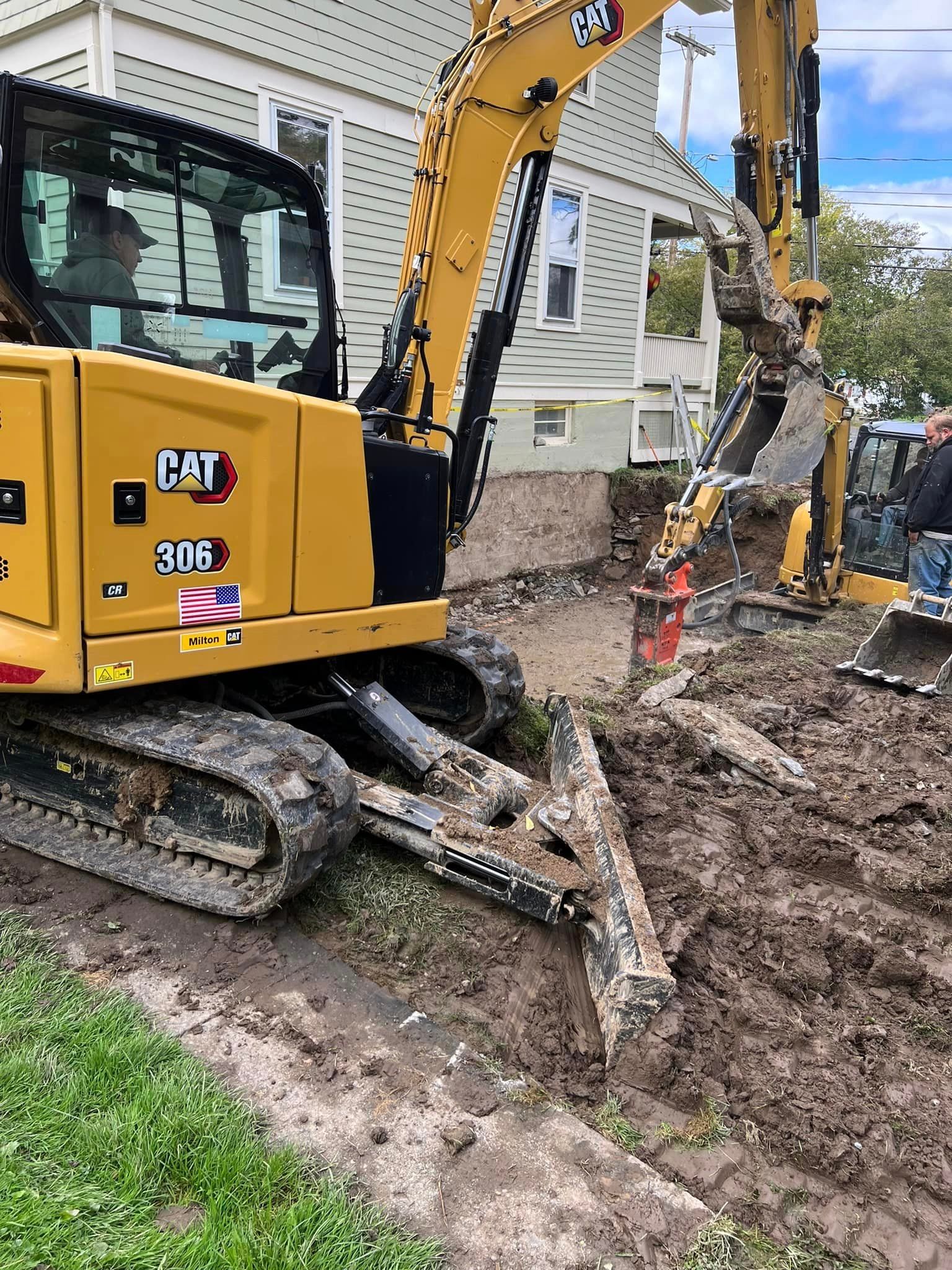 A yellow excavator is digging a hole in the dirt in front of a house.