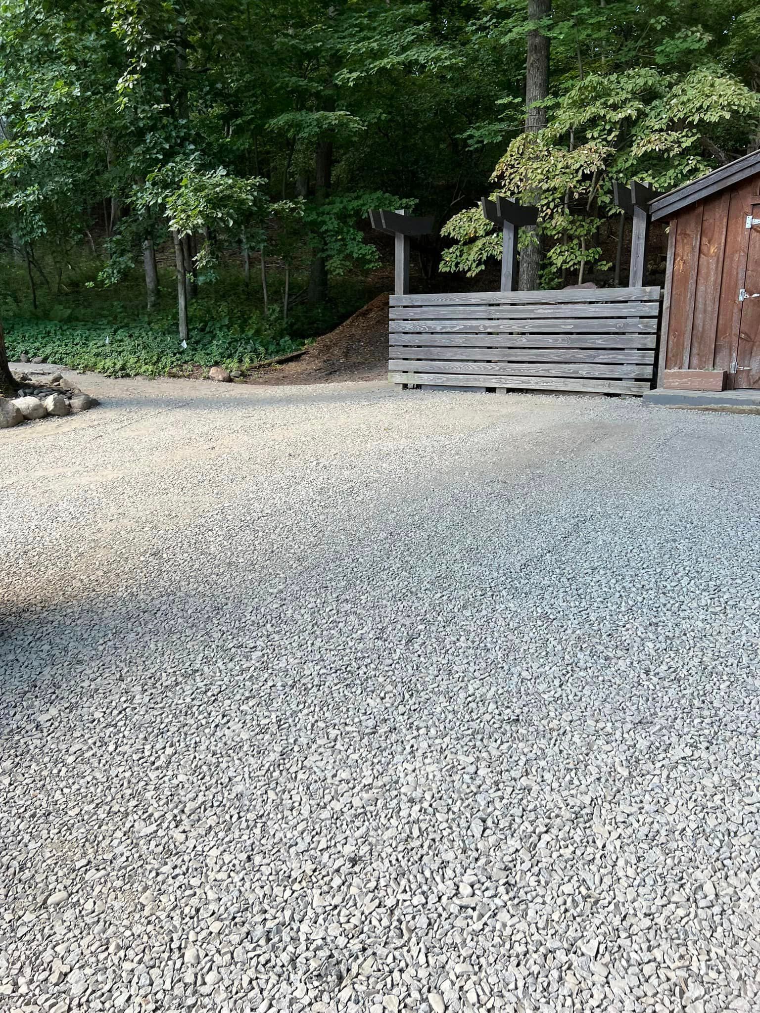 A gravel driveway with a wooden fence and trees in the background.
