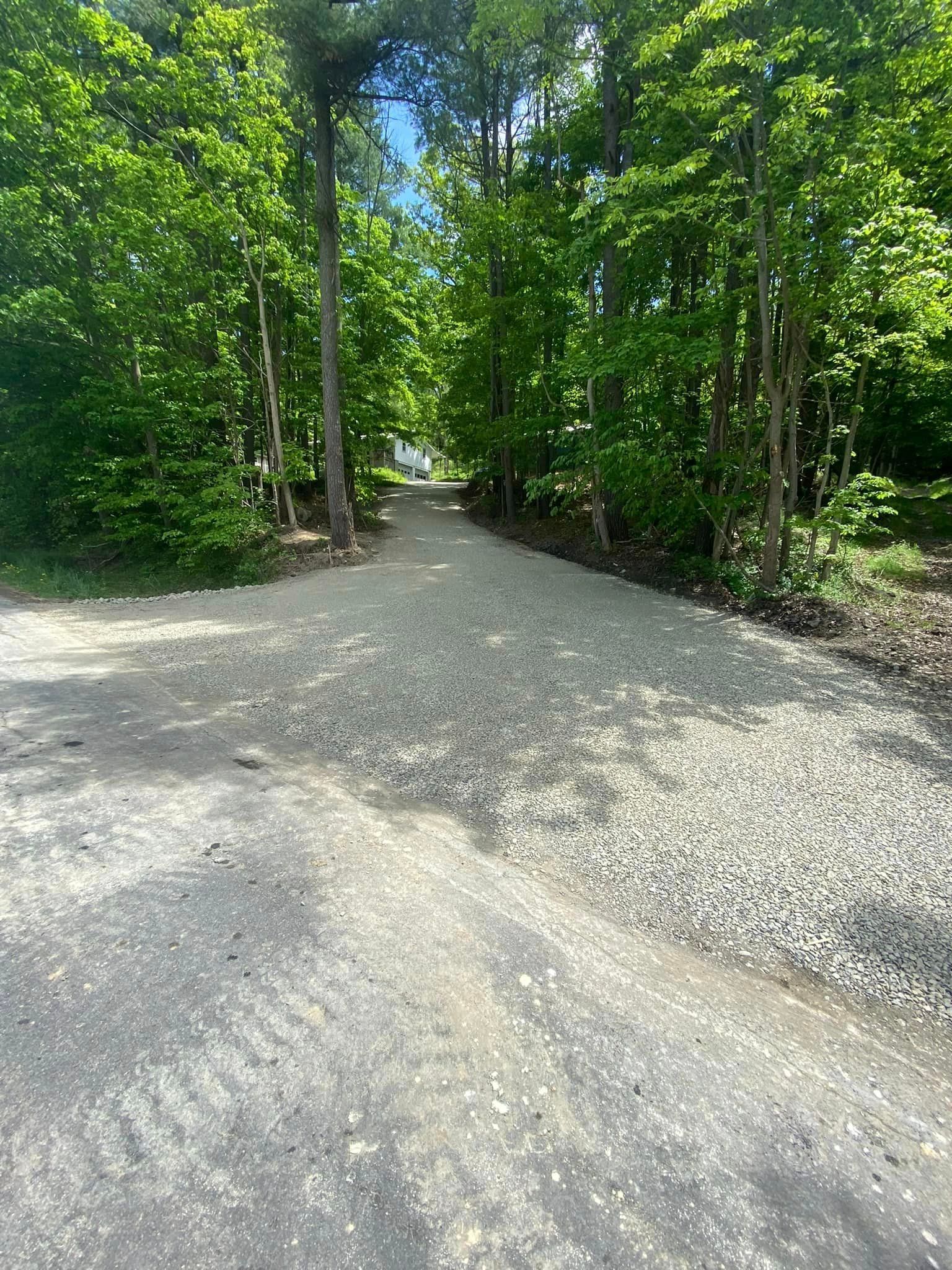 A gravel road going through a forest with trees on both sides.