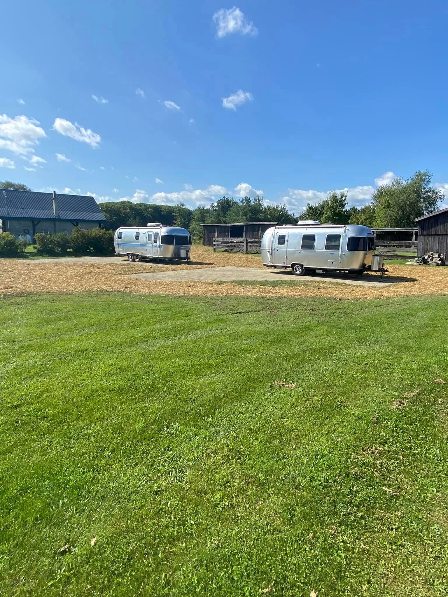 Two airstream trailers are parked in a grassy field.