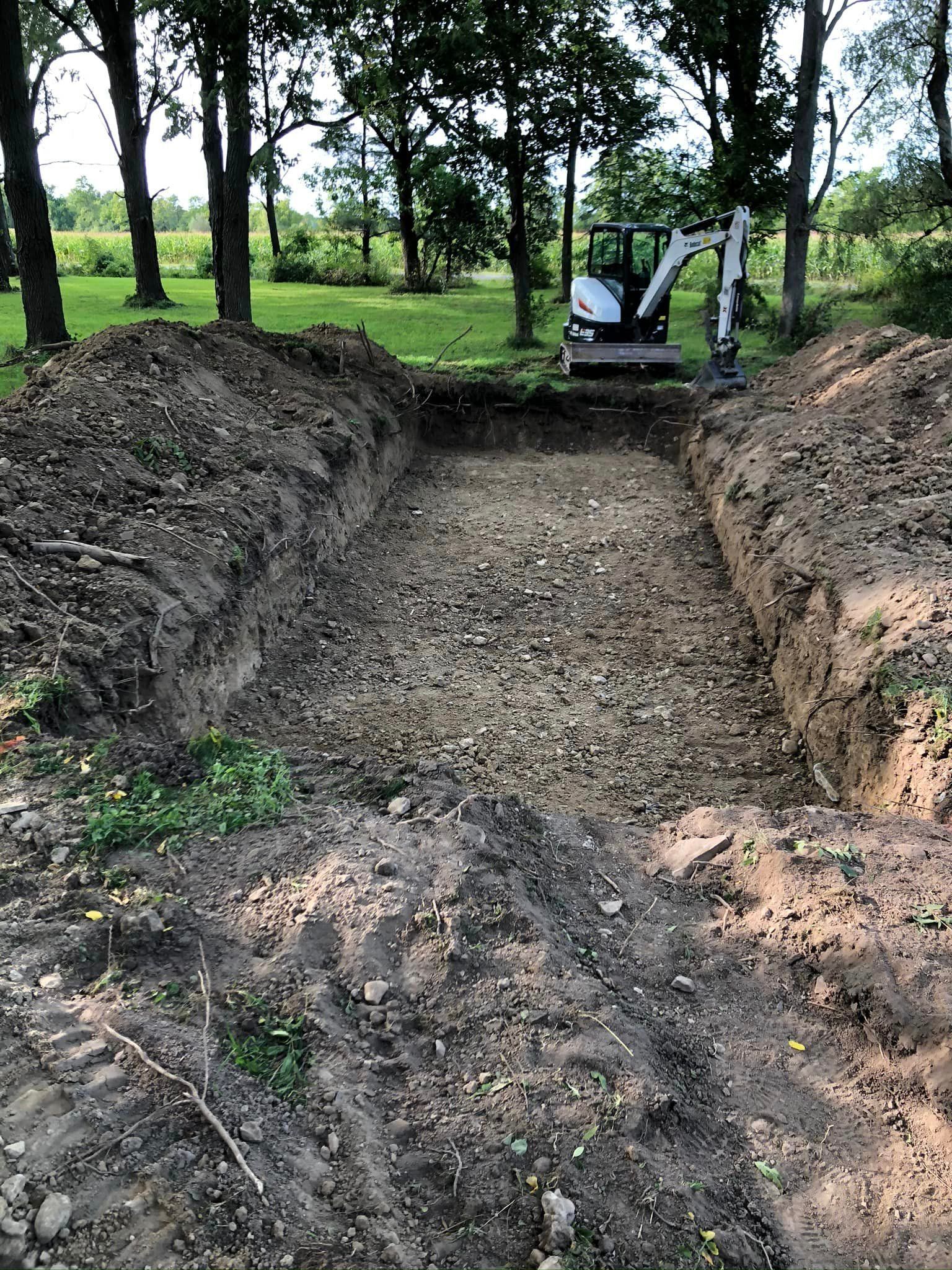 A bulldozer is digging a hole in the dirt in the middle of a forest.