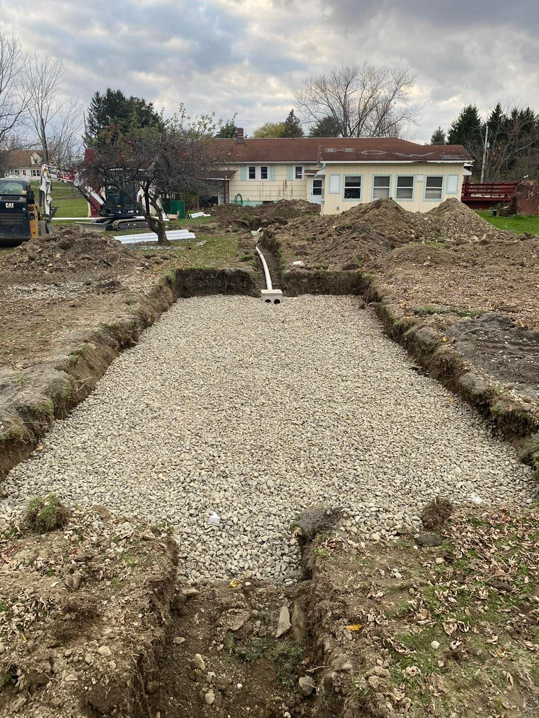 A large pile of gravel is sitting in the middle of a dirt field in front of a house.