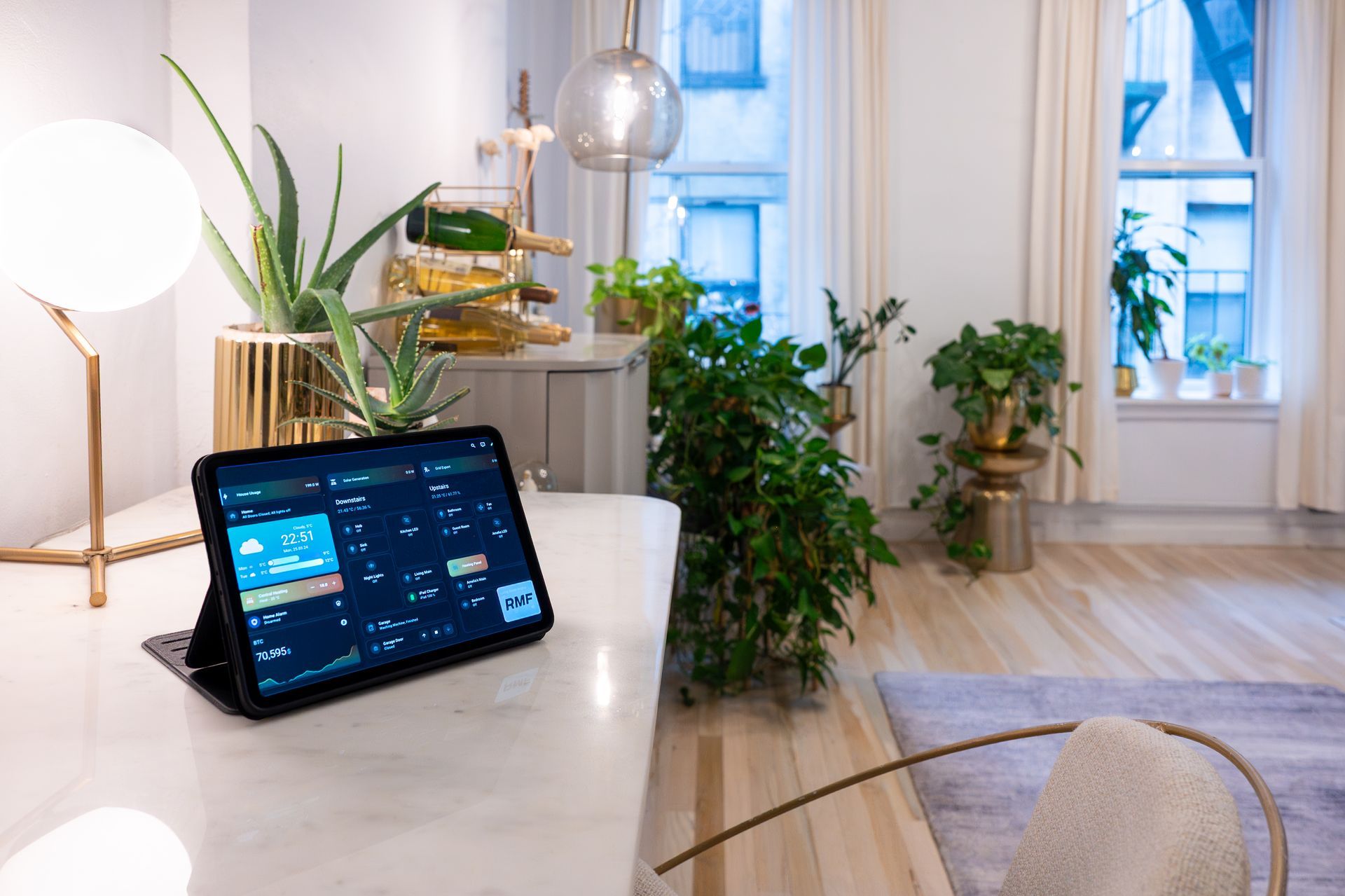 Tablet on marble countertop in a modern home, showing a smart home interface. Lush plants and natural light.