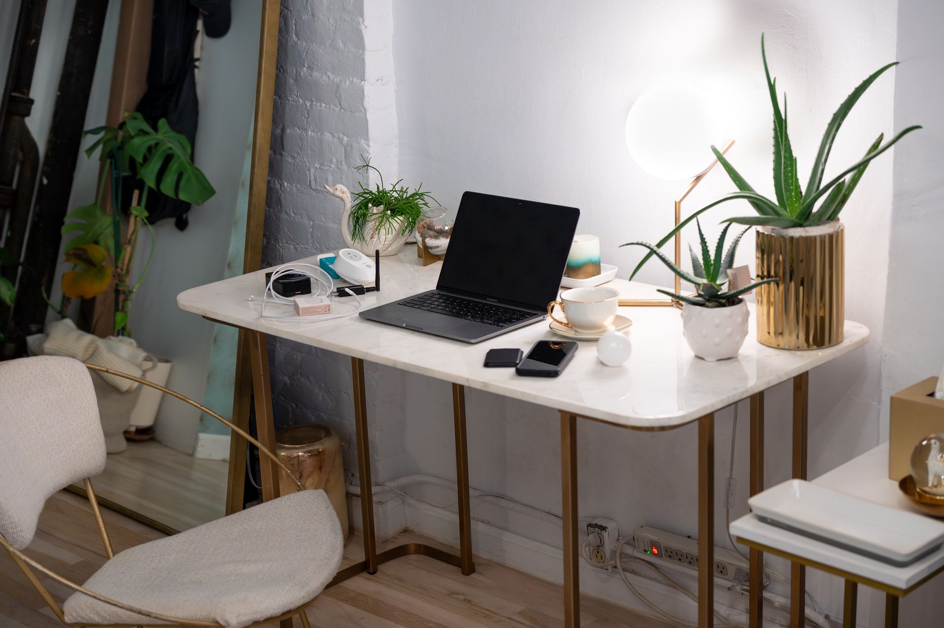 A minimalist home office with a laptop, aloe plants, a desk, and a chair.