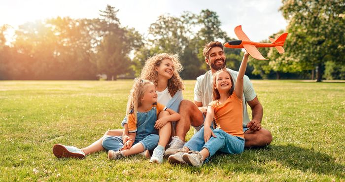 Family of four in a sunny park, playing with a toy airplane.