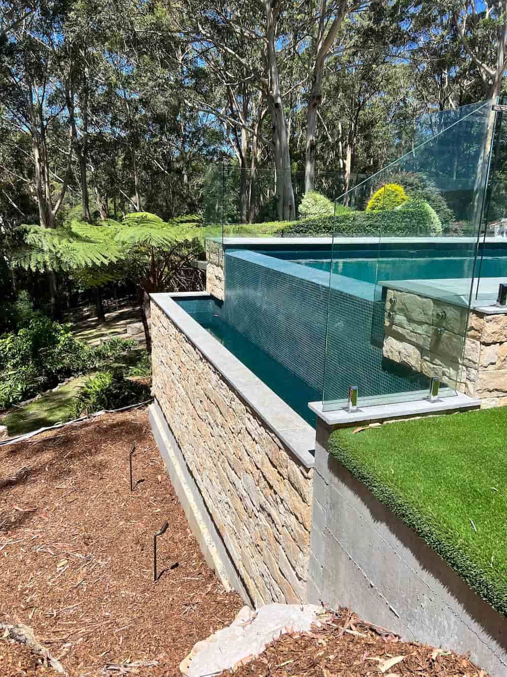 A Large Swimming Pool Is Surrounded By A Stone Wall And Trees — ASpect Wall & Floor Tiling in Forster, NSW