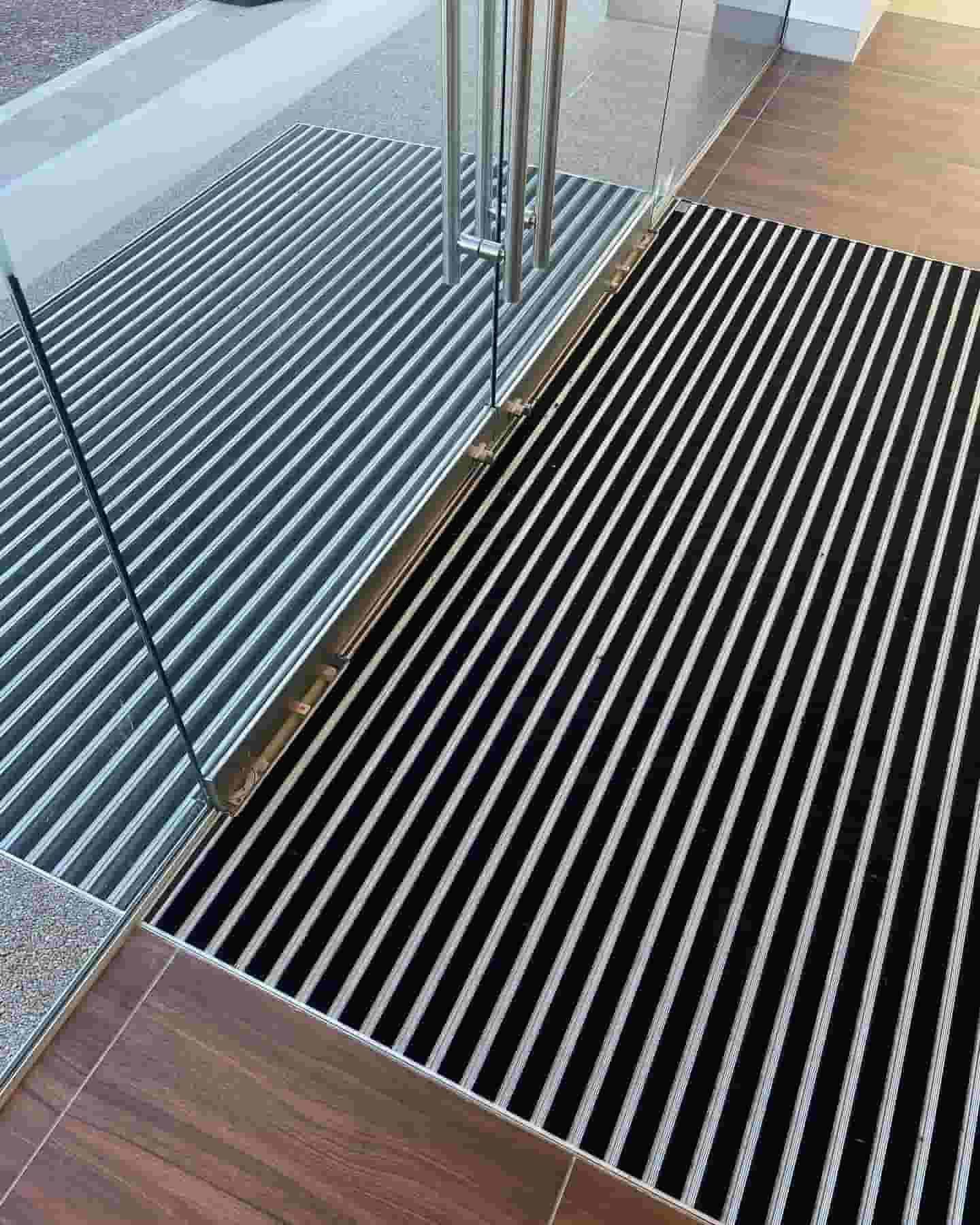 A Black and White Striped Mat is on the Floor in Front of a Glass Door — ASpect Wall & Floor Tiling in Charmhaven, NSW
