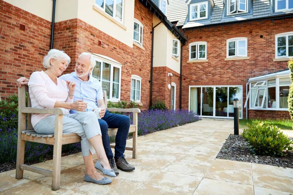 An Elderly Couple is Sitting on a Bench in Front of a Brick Building — ASpect Wall & Floor Tiling in Charmhaven, NSW