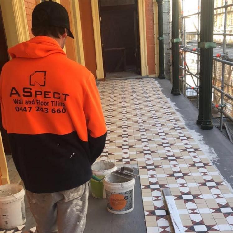 A Man Wearing an Orange Jacket That Says Aspect on the Back — ASpect Wall & Floor Tiling in Charmhaven, NSW