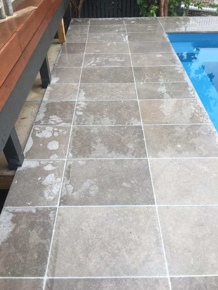 A Tiled Floor Next to a Swimming Pool With a Wooden Bench — ASpect Wall & Floor Tiling in Sydney, NSW