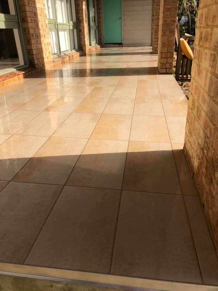 A Patio With Tiles and a Brick Wall in Front of a House — ASpect Wall & Floor Tiling in Charmhaven, NSW
