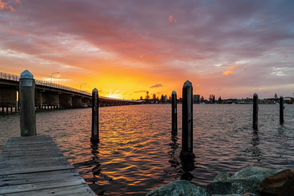 A Dock Overlooking a Body of Water With a Bridge in the Background at Sunset — ASpect Wall & Floor Tiling in Tuncurry, NSW