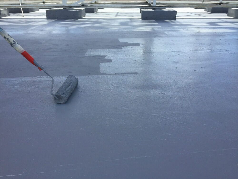 A Person is Painting a Concrete Floor With a Roller — ASpect Wall & Floor Tiling in Charmhaven, NSW