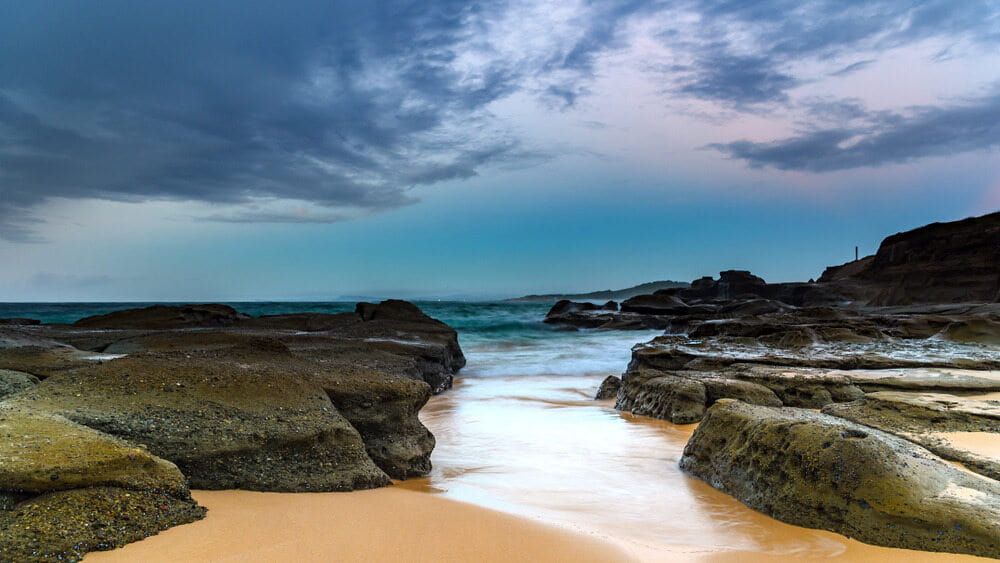 A Beach With Rocks and Waves Coming in on a Cloudy Day — ASpect Wall & Floor Tiling in Wyong, NSW