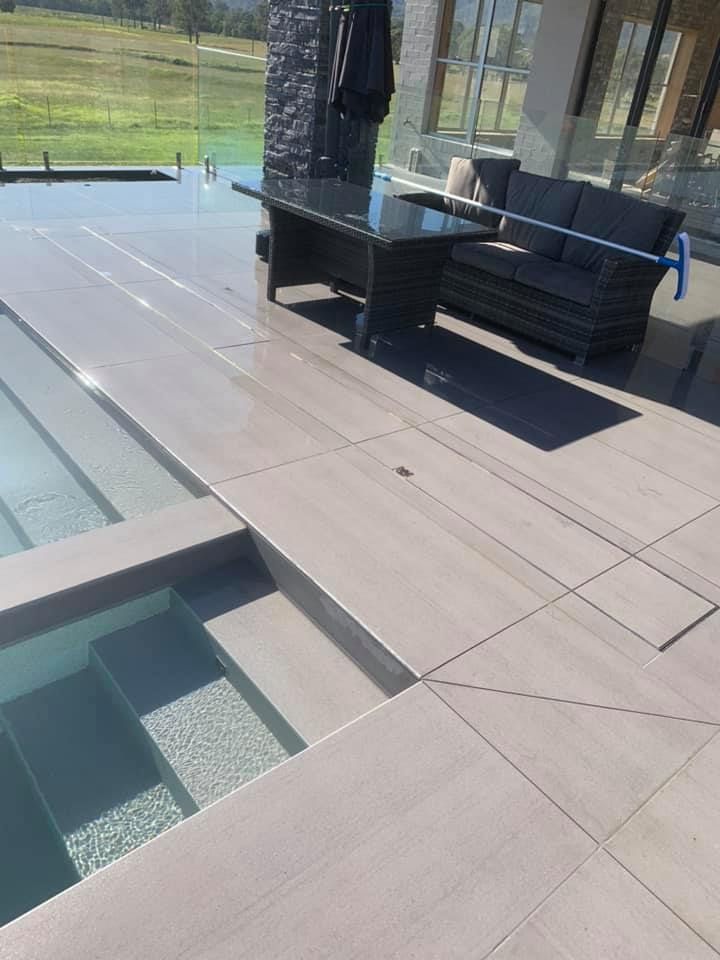 A Patio With a Couch , Table and Chairs Next to a Pool — ASpect Wall & Floor Tiling in Forster, NSW