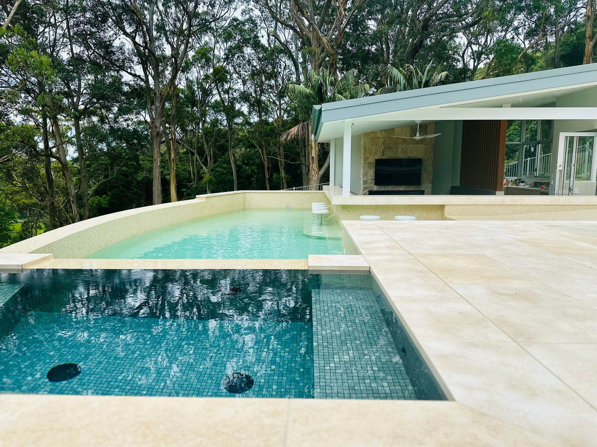 A Large Swimming Pool is Surrounded by Trees and a House β ASpect Wall & Floor Tiling in Charmhaven, NSW