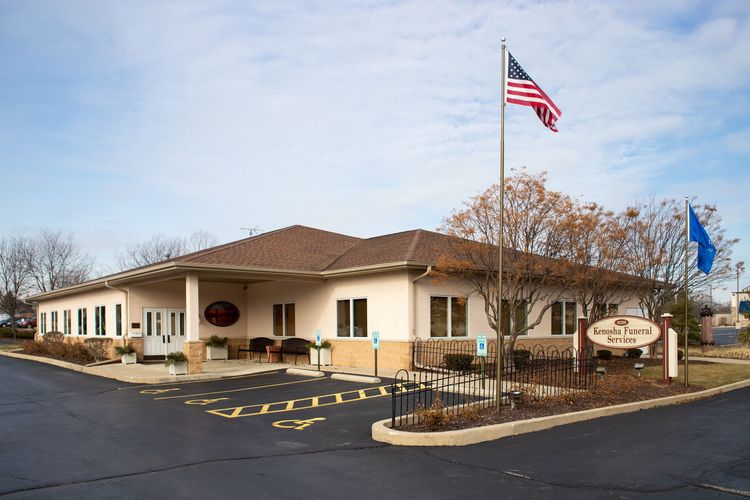 A beige, single-story professional building with a shingled roof, handicap parking spots, and two flagpoles on a clear day.