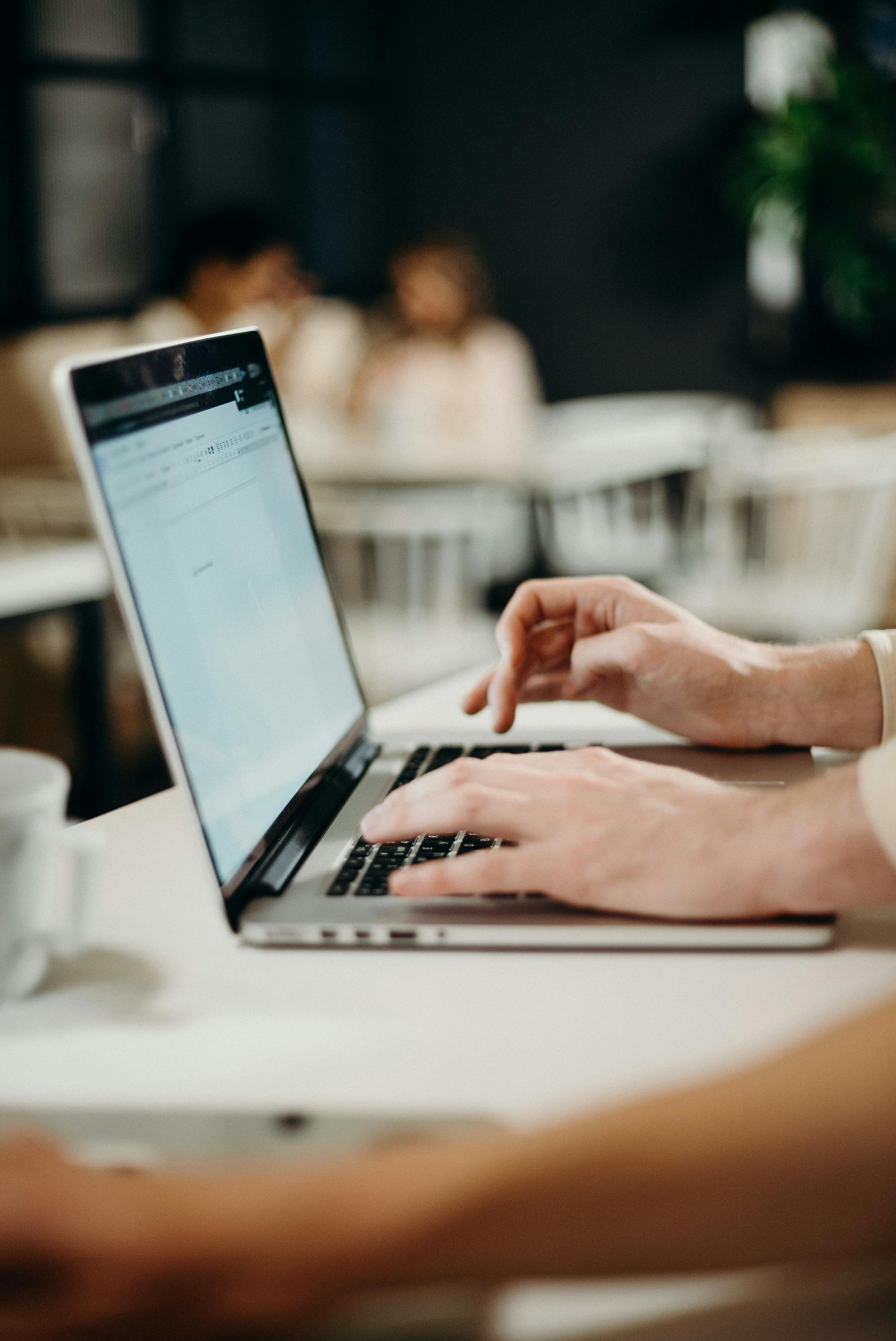 A person typing on a laptop in a blurred, brightly lit office setting.