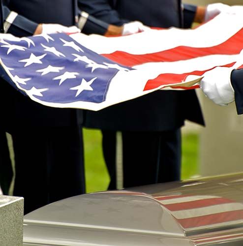 Military personnel in dress uniforms holding a folded American flag over a casket at a graveside service.