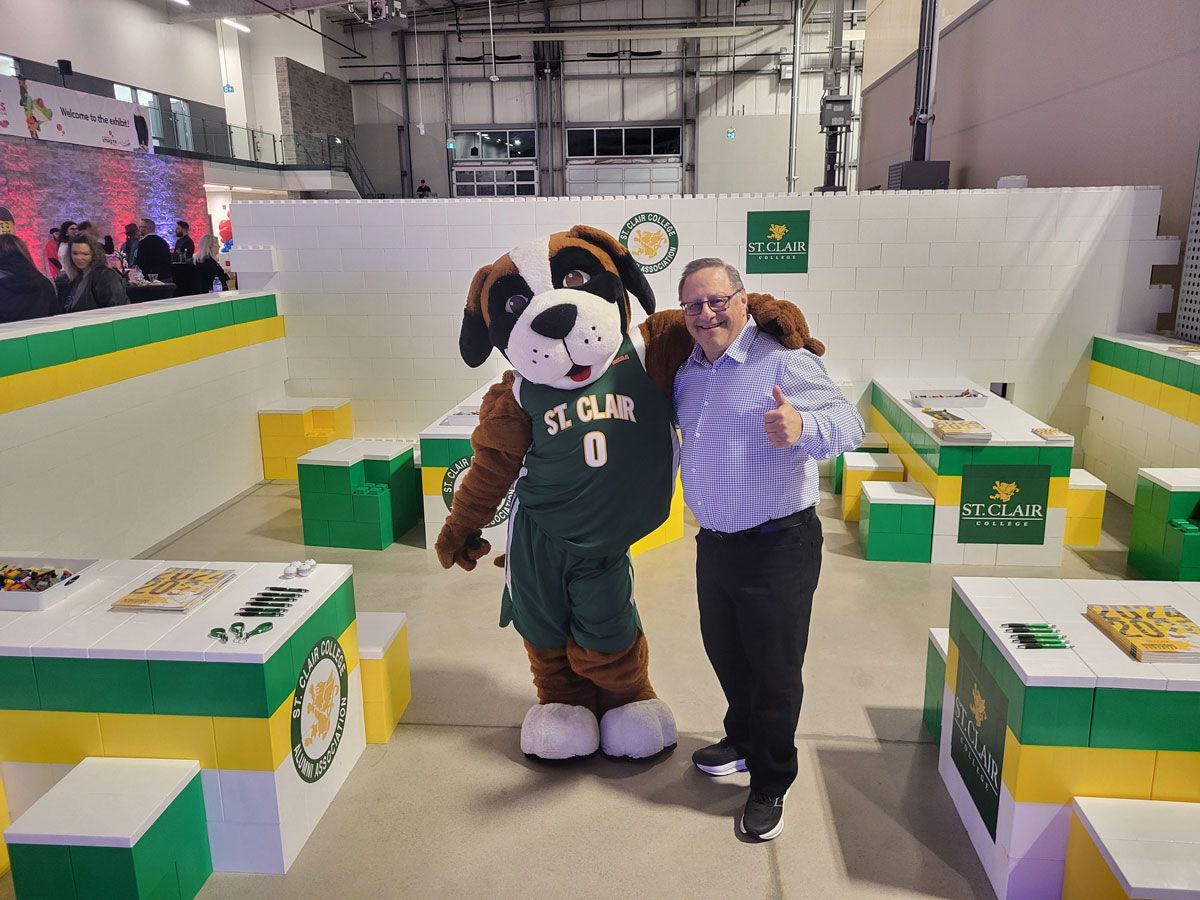 A man is standing next to a mascot wearing a st. cloud jersey