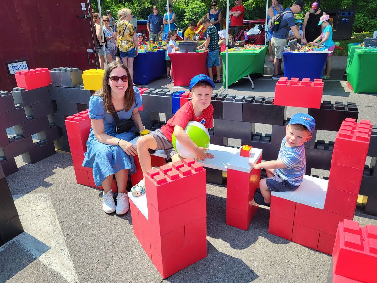 A woman and two children are sitting on chairs made out of lego blocks.