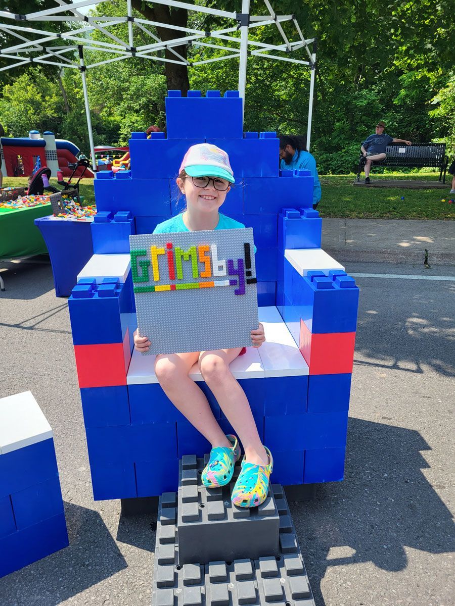 A little girl is sitting in a chair made out of lego blocks
