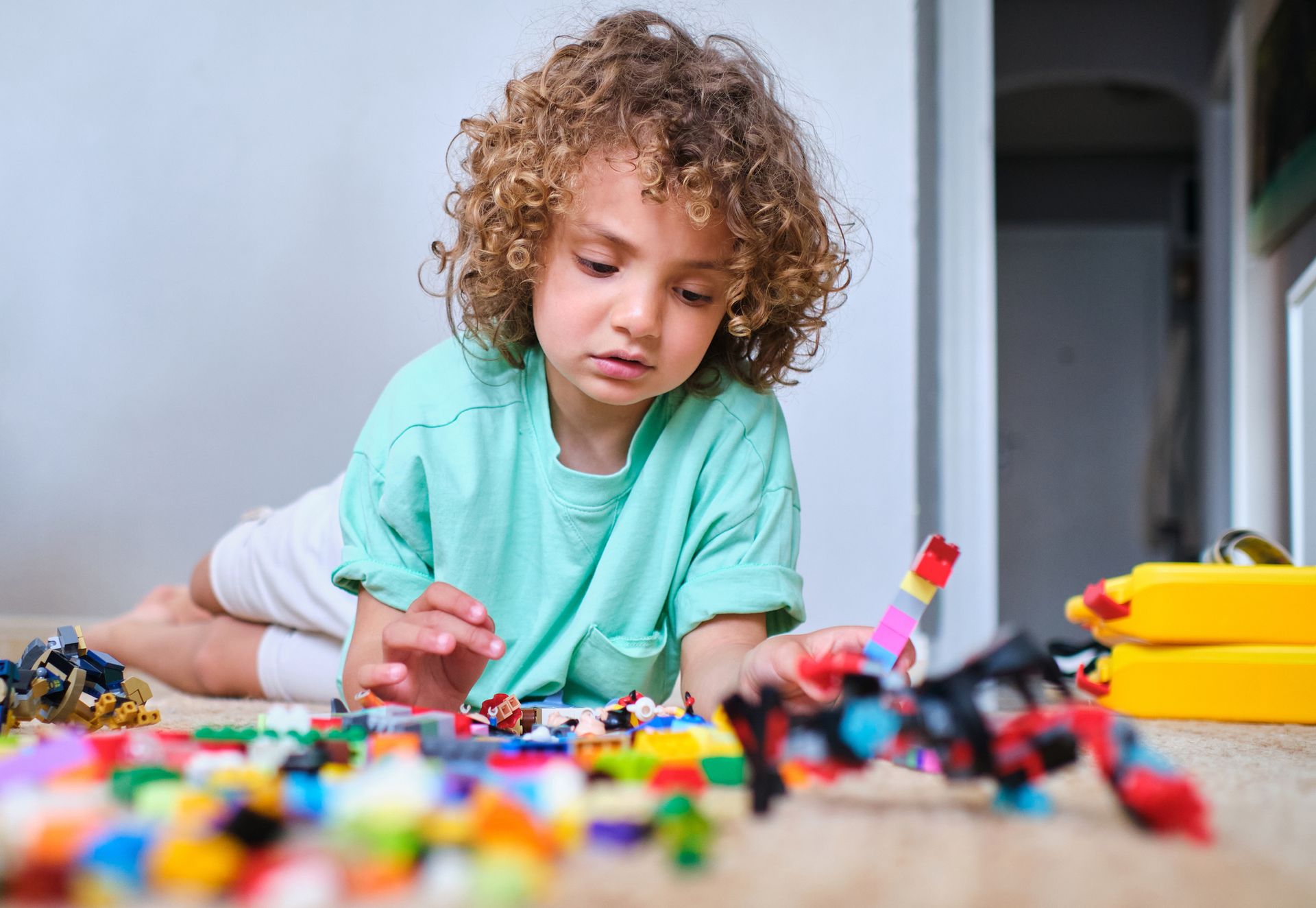 A young boy is laying on the floor playing with lego blocks.