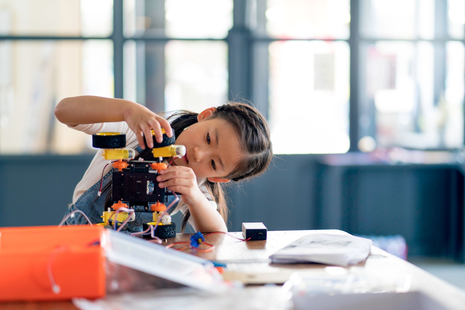 A young girl is sitting at a table playing with a toy robot.