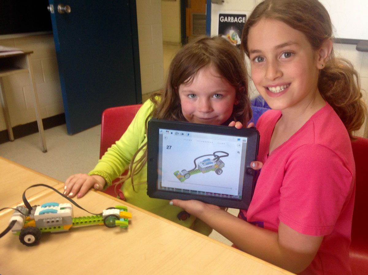 Two young girls are sitting at a table holding a tablet.