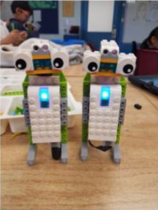 Two lego robots are sitting on a wooden table