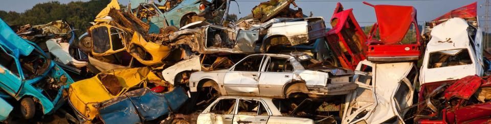 A large, cluttered pile of colorful, wrecked and salvaged cars at a scrapyard under a clear blue sky.