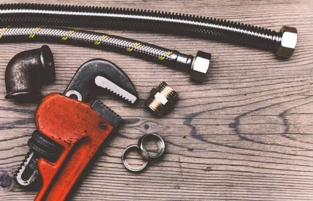 A plumber 's wrench and hose are on a wooden table.