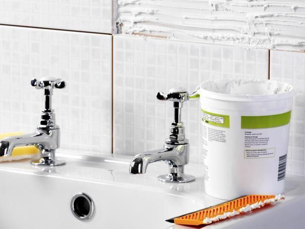 A bathroom sink with two faucets and a bucket of glue